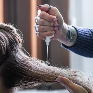 Produkt ściśnięty w ręce fryzjerki rozprowadza na włosy regenerującą zawartość